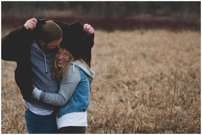 A couple shares a warm embrace under a coat in a r
