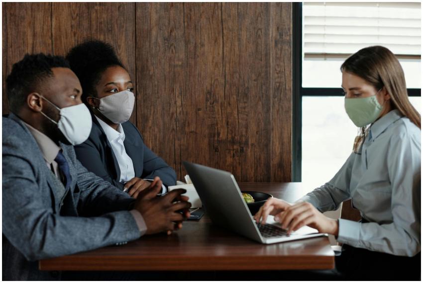 Three business professionals in masks discussing a