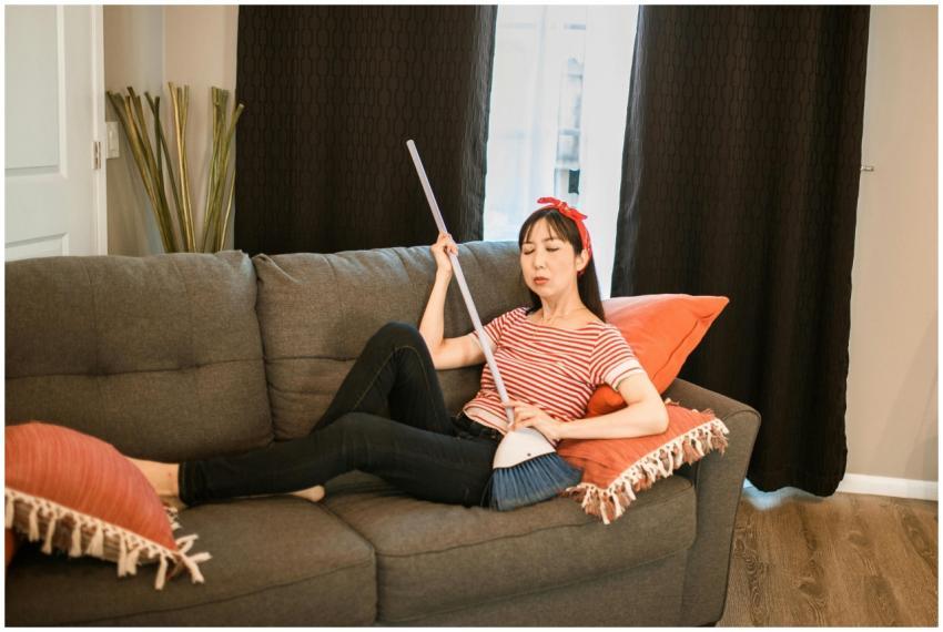 Woman lounging on a sofa holding a broom, in a coz