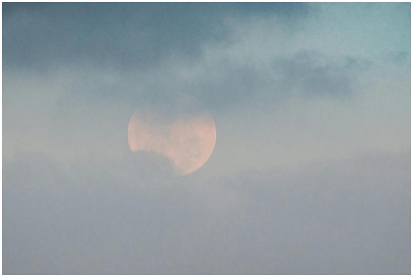 White moon showing through thick clouds on blue sk