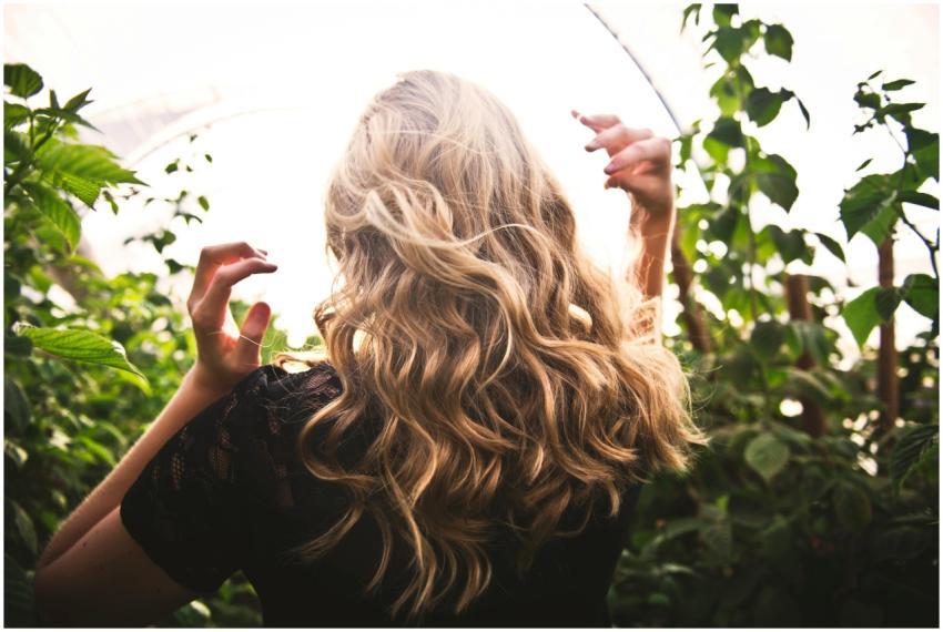 Blonde woman with curly hair surrounded by lush gr