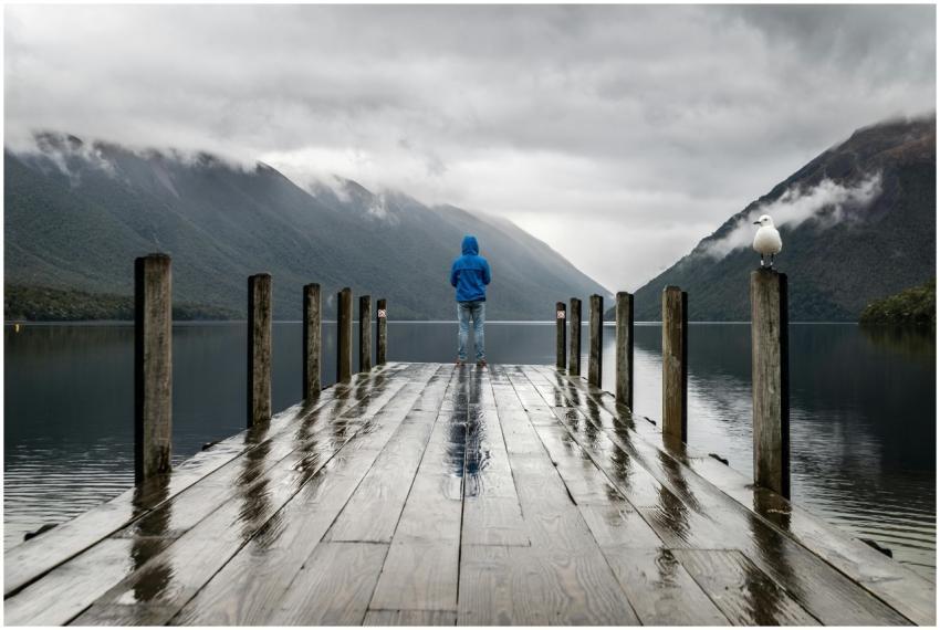 Person in blue jacket stands on a rainy dock overl