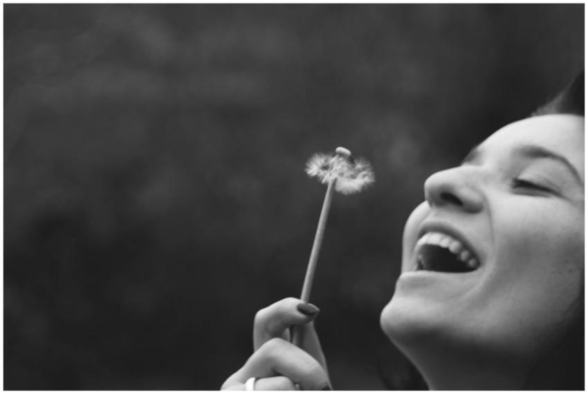 A joyful woman smiling while blowing on a dandelio