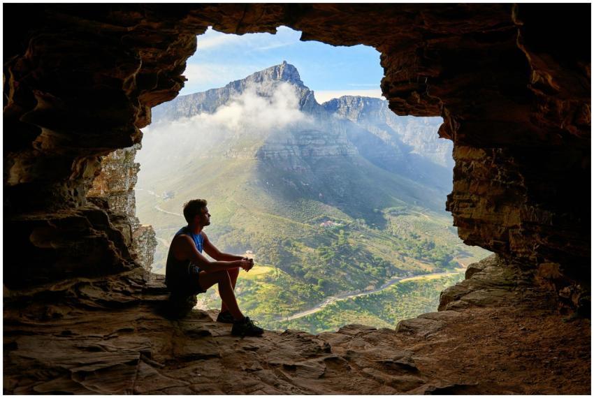 A man sitting in a cave overlooking a majestic mou