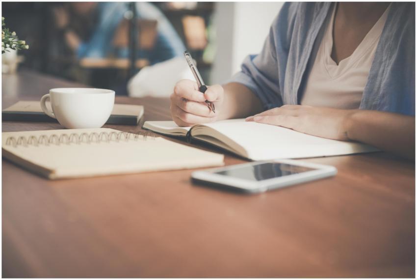 A woman writes in a notebook at a café table with
