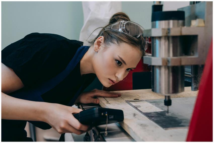 Woman closely inspecting machinery in a workshop w