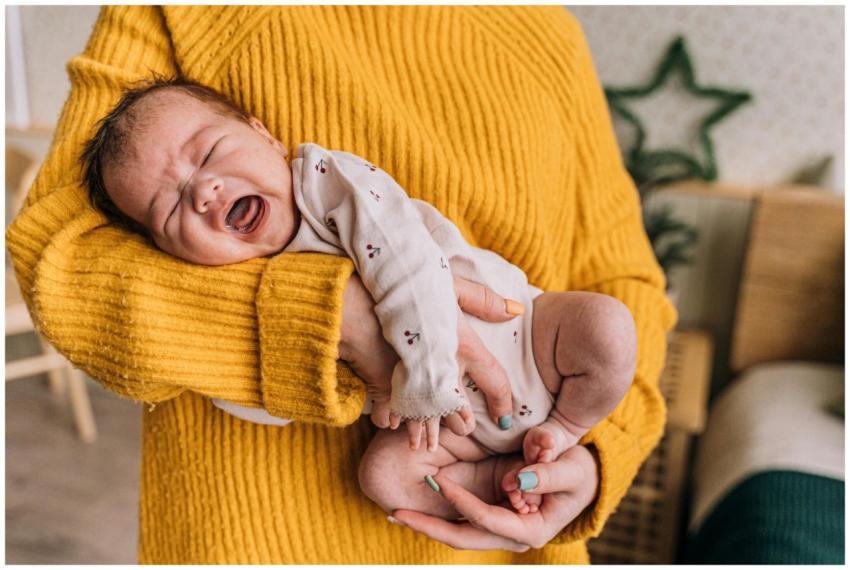 A mother gently holds a crying baby in her arms, p