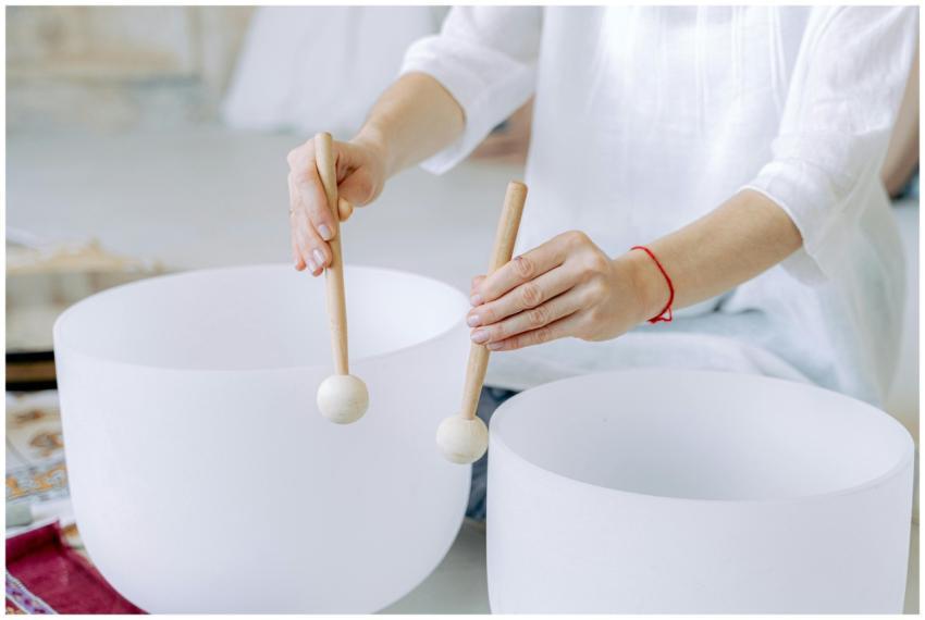Hands playing crystal singing bowls with mallets,