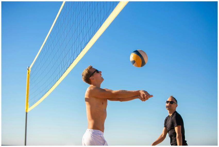 Men playing volleyball on a sunny beach with a cle