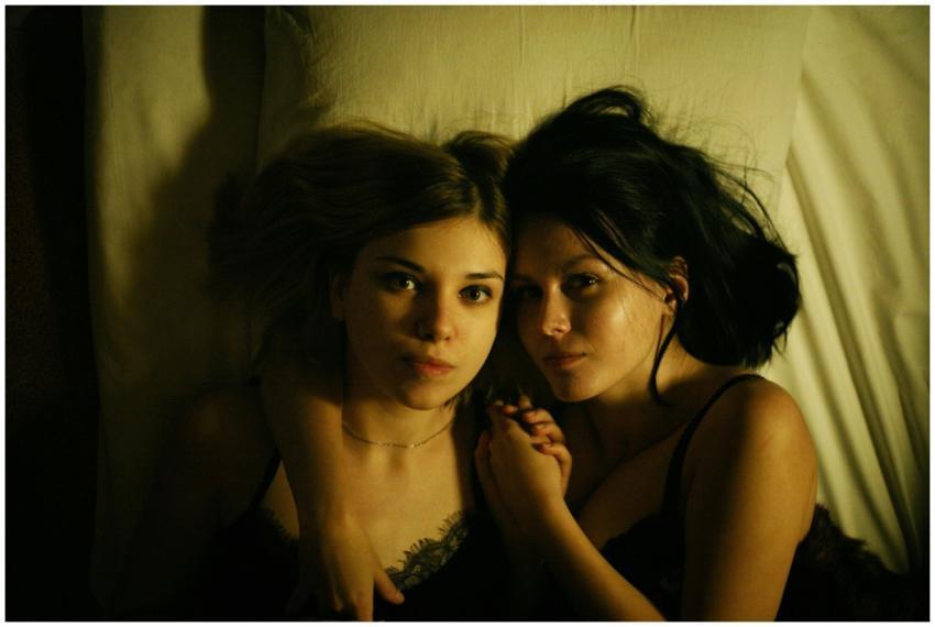 Two women lying in bed, holding hands, sharing an