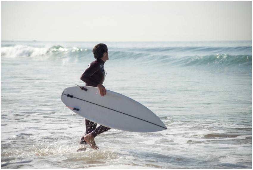 A surfer holding a surfboard walks into the ocean