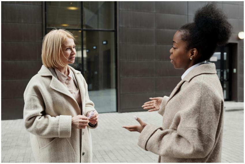 Two businesswomen in coats converse outside a mode