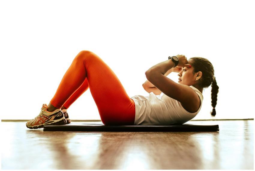 Side view of a young woman doing sit-ups on a mat,