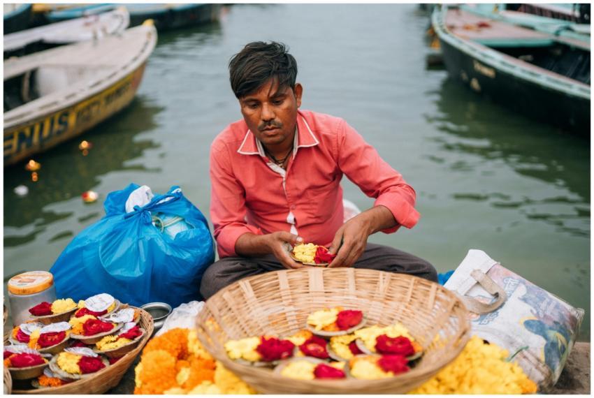 Man arranging flower offerings by the Ganges in Va