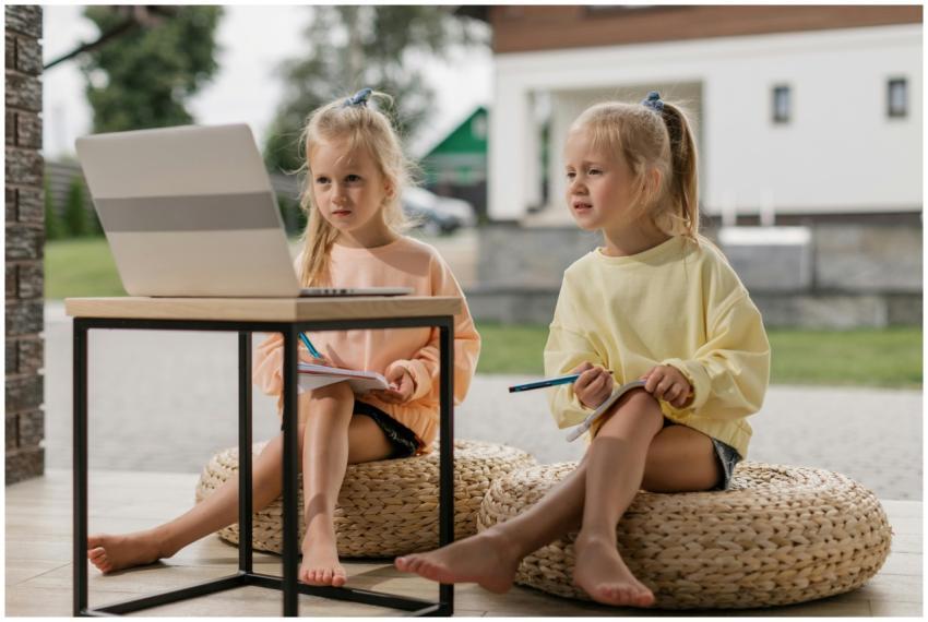 Twin girls studying online with a laptop outdoors,