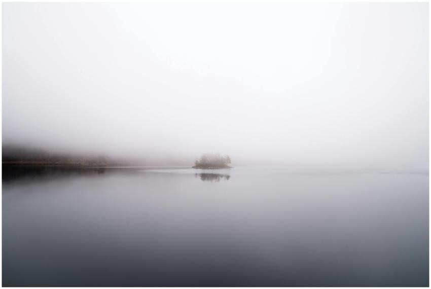 A tranquil misty lake scene with an island reflect