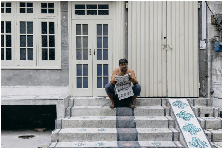A man sitting on stairs reading a newspaper in fro