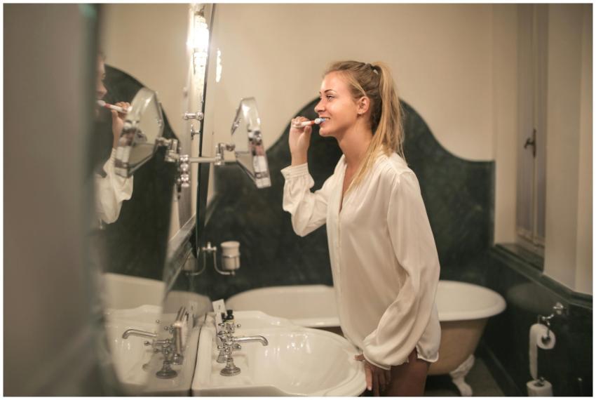 A cheerful young woman in a bathroom brushing her