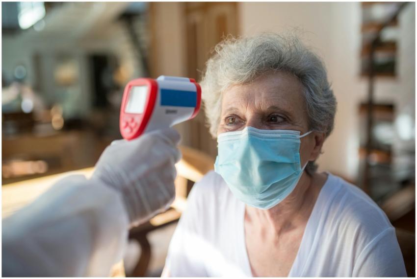A senior woman wearing a mask receives a temperatu