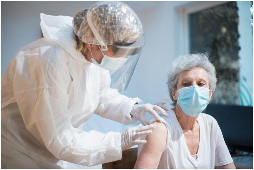 Nurse in protective gear giving vaccine to senior