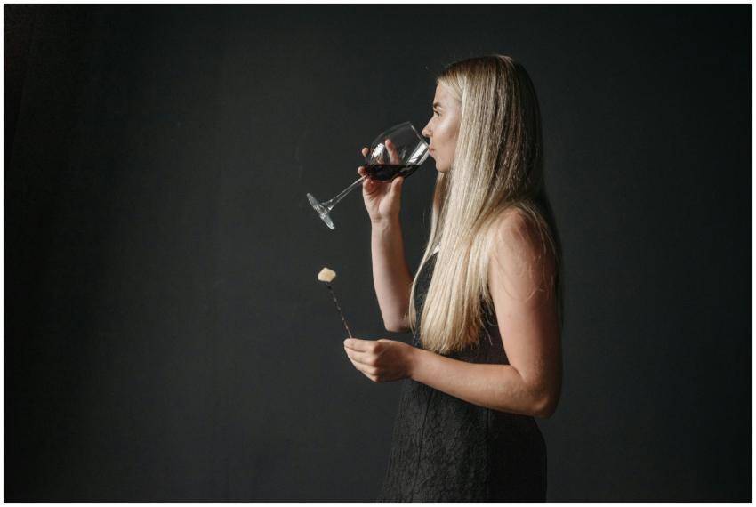 Blonde woman savoring red wine while holding chees