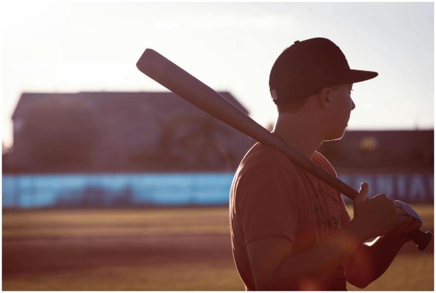 A teenage boy holding a baseball bat looks towards