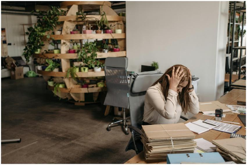 A stressed woman sits overwhelmed at her desk, sur