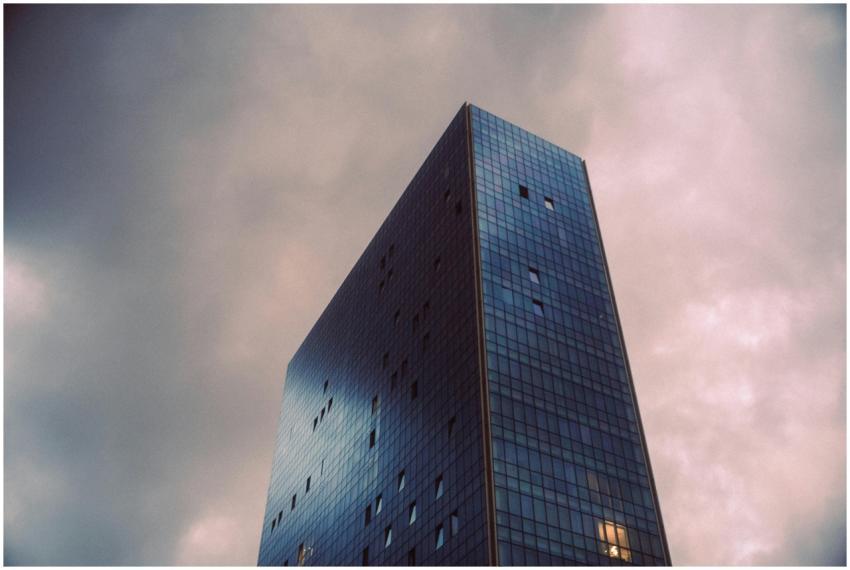 A towering modern glass skyscraper against a moody