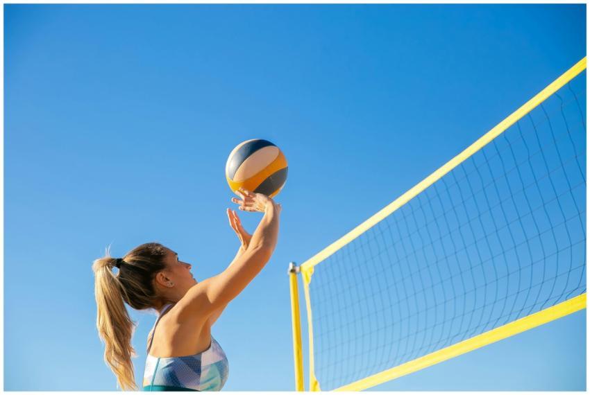 A woman plays volleyball on a sunny day, reaching
