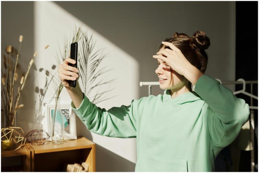 A young girl in a green hoodie takes a selfie indo