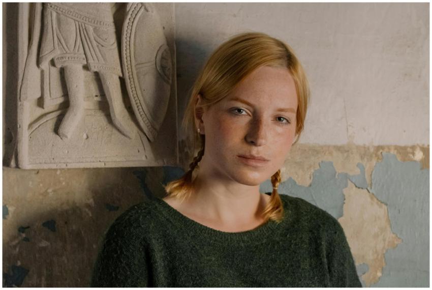 A redheaded woman with pigtails posing against a r