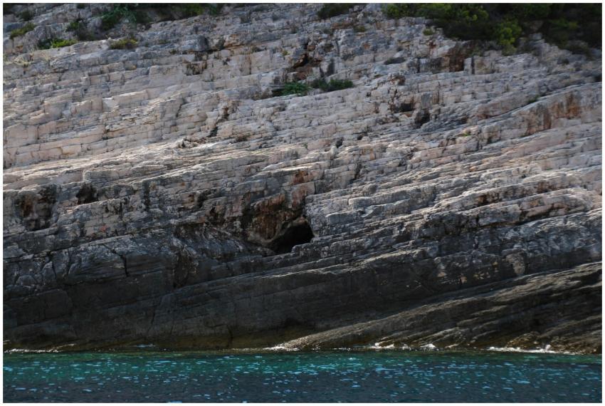 A rugged rocky cliff beside a calm azure sea, capt