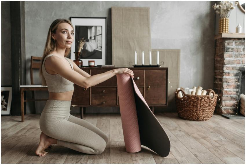 Woman in sportswear rolling a yoga mat in a cozy h