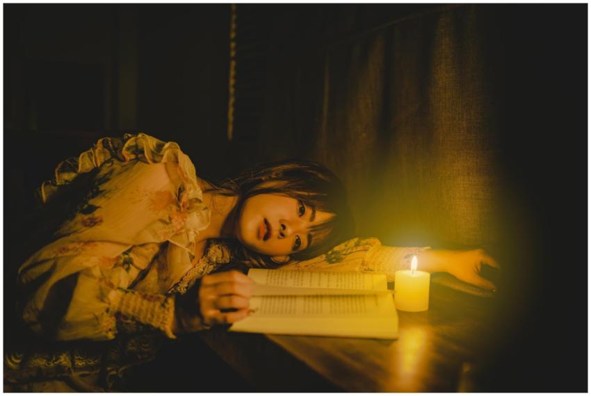 A woman reading a book by candlelight, creating a