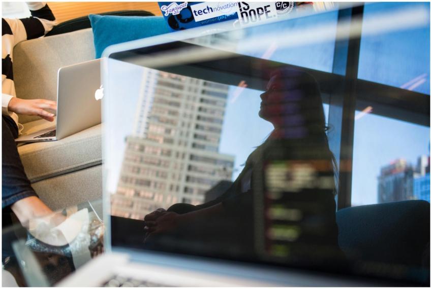 A woman is reflected on a laptop screen displaying