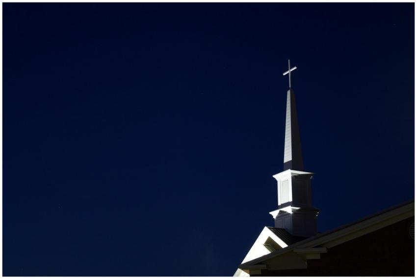 Illuminated church steeple with cross at night. Pe