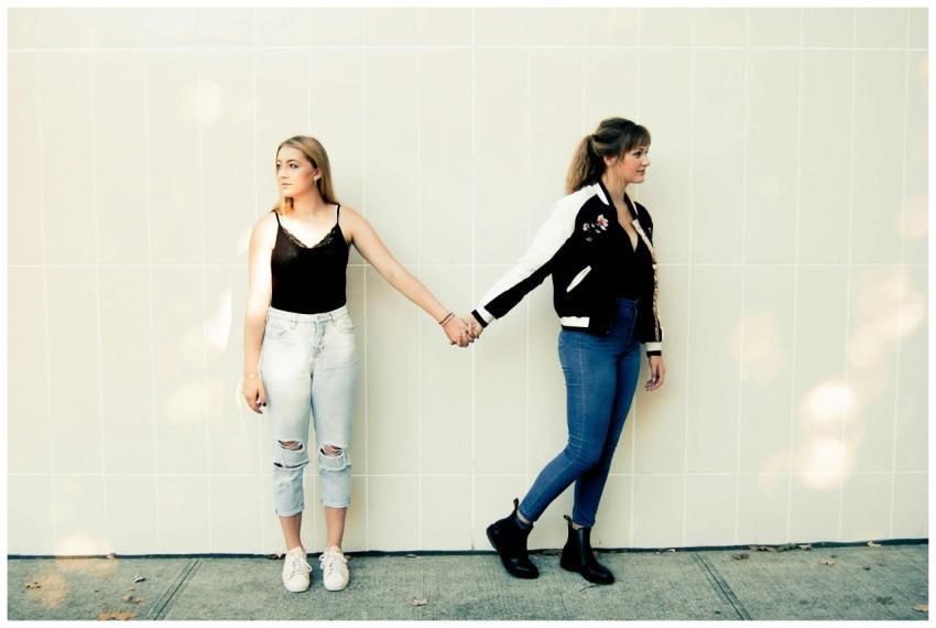 Two young women in casual outfits holding hands ag