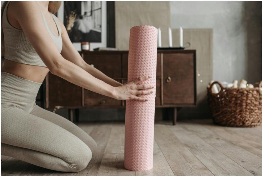 A woman in activewear unrolls a pink yoga mat indo