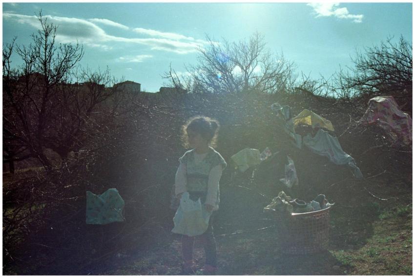 A young child stands in the sunny outdoors of Heki