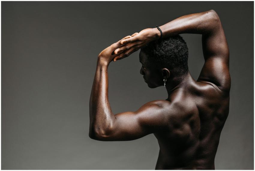 A strong shirtless man poses with arms overhead in