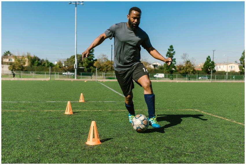 Adult soccer player warming up with cones on a sun