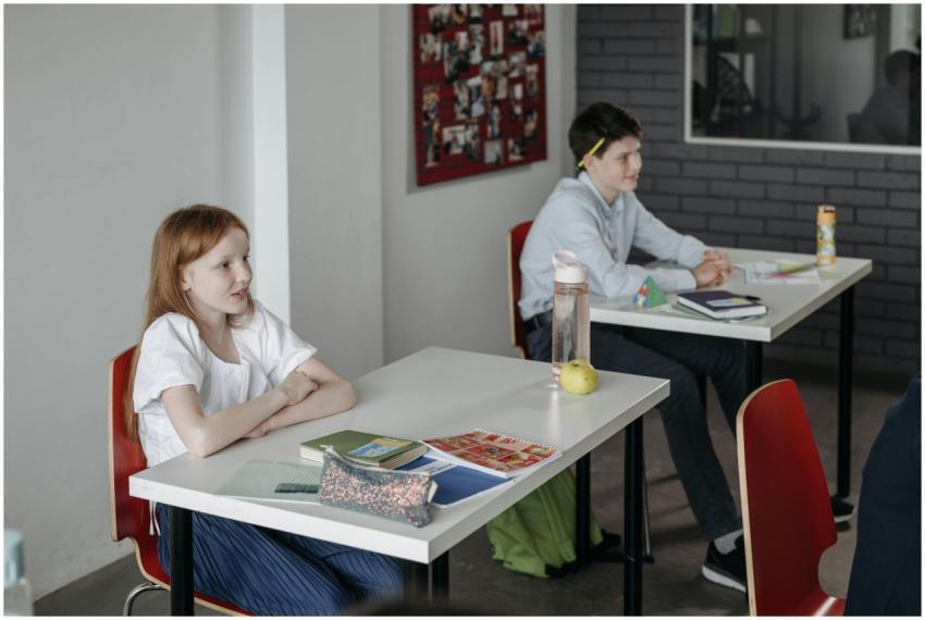 Two children sitting at desks in a classroom, enga