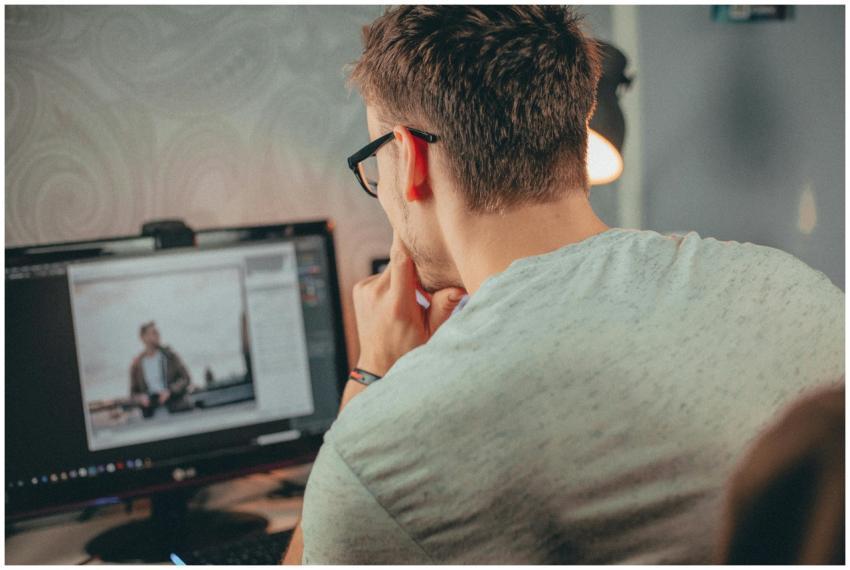 A man with glasses focused on editing a photo on h