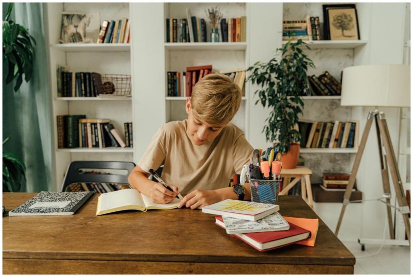 A young boy writes in a notebook at a desk surroun