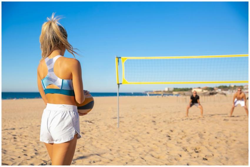 A woman plays beach volleyball under a clear blue