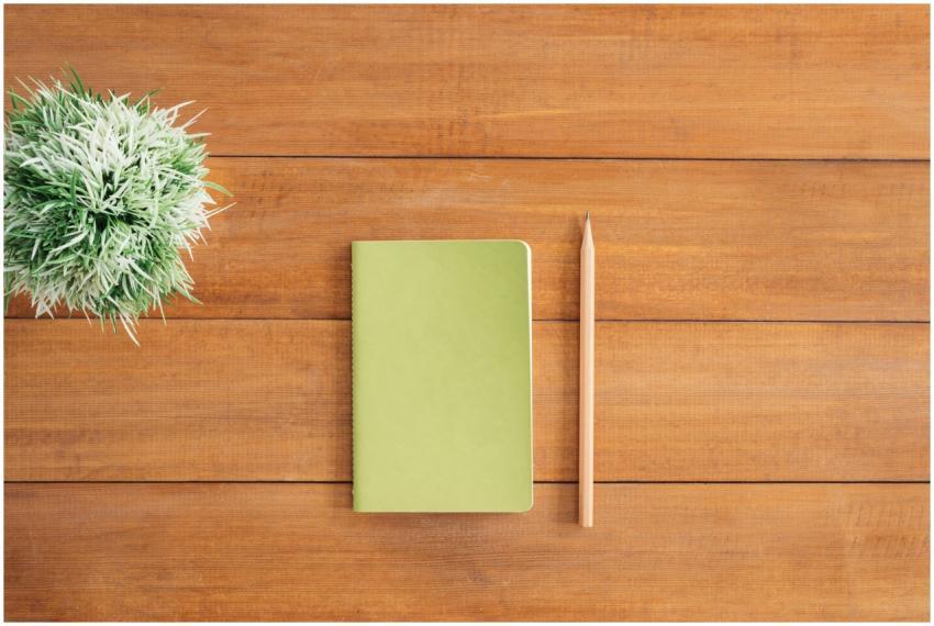 Flat lay of green notebook and pencil on wooden de