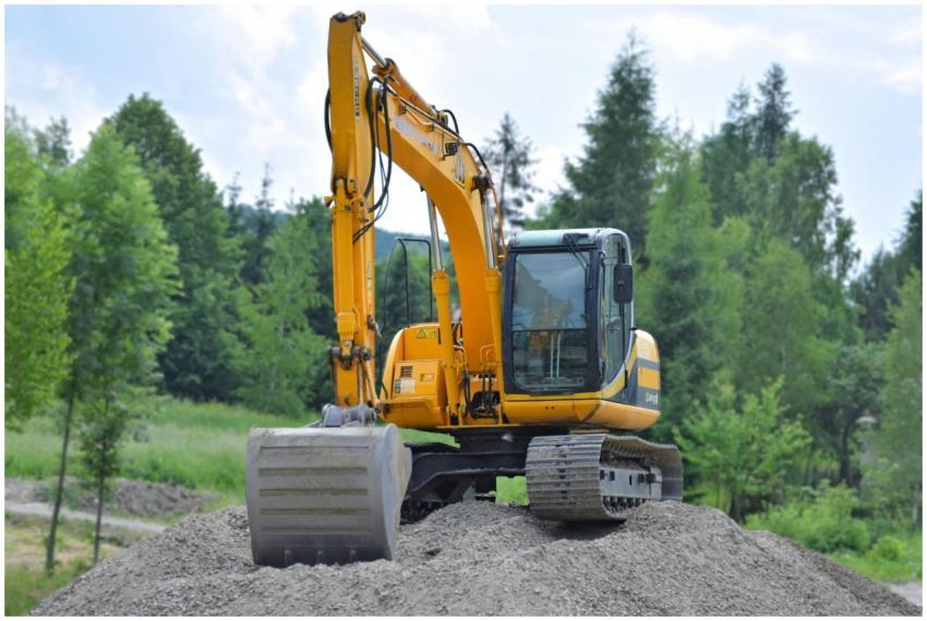 A yellow excavator on a pile of gravel in a lush,
