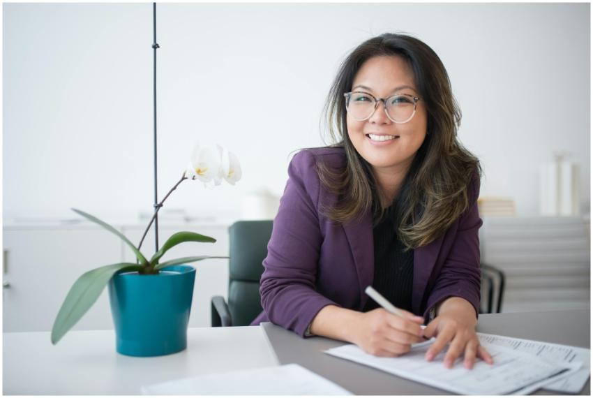 Asian woman with glasses smiles while working at a
