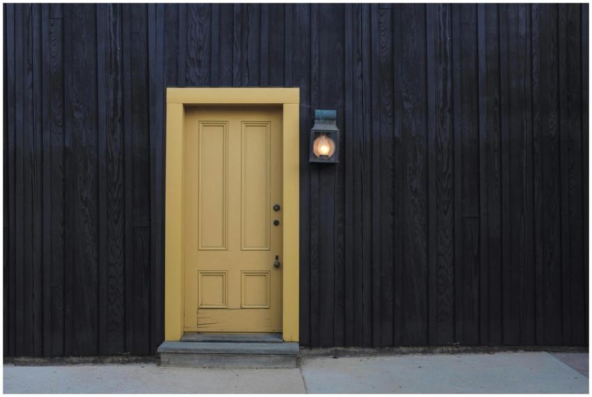 A modern yellow door on a dark wooden facade creat