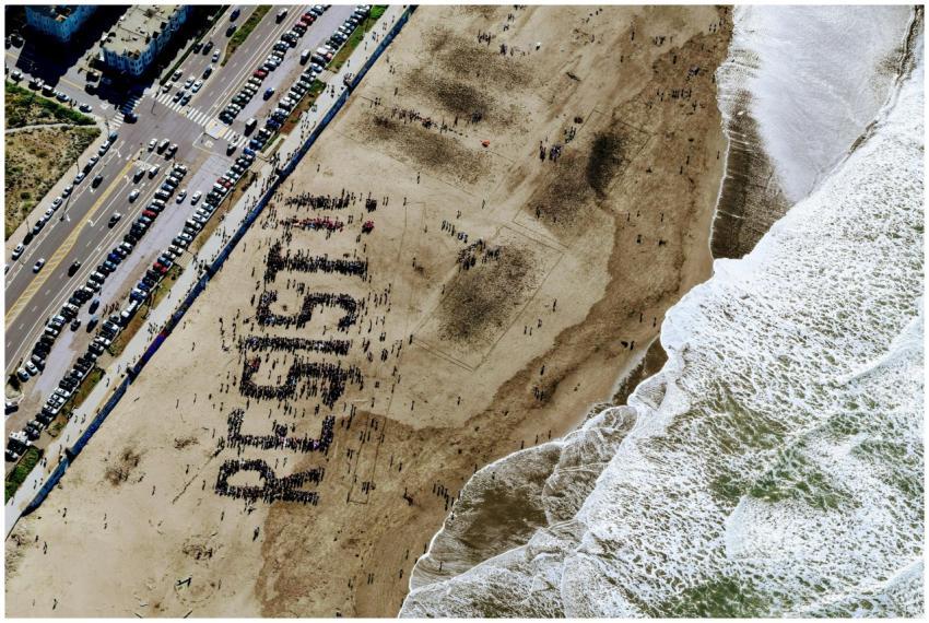 A large group on a beach forms the word "Resist" i